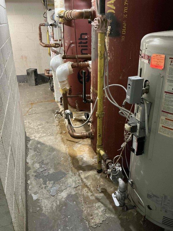 Conducted on-site assessment for domestic hot water boiler replacement in basement utility area. Evaluated existing aged maroon boiler tank and white water heater unit, noting deteriorated condition with visible corrosion, mineral deposits, and floor staining indicating previous water damage. Documented current copper piping configuration, insulation condition, gas valve locations, and electrical connections. Provided comprehensive estimate for replacement of domestic hot water boiler system.