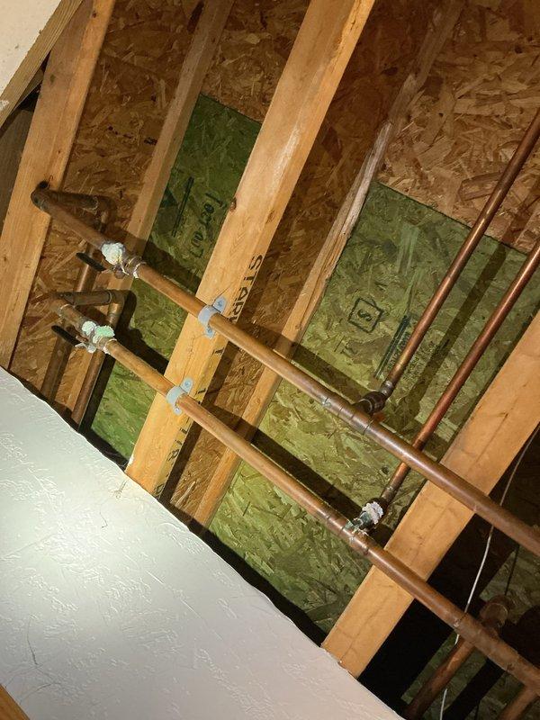 Responded to water leak complaint affecting two areas: basement ceiling and main floor. Performed diagnostic inspection and accessed wall cavity to locate source of leak. Identified compromised copper plumbing lines running through wall structure between floors. Removed section of drywall to expose framing, insulation, and copper piping for proper assessment and repair access. Secured copper pipes with appropriate mounting brackets and addressed leak points. Documented conditions with photos showing ceiling texture damage, exposed wall framing with fiberglass insulation, and copper pipe routing through stud cavities.