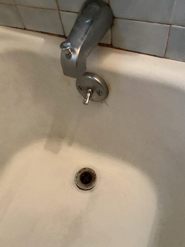 Responded to service call for clogged drain in 1950s-era home. Upon inspection, identified obsolete drum trap configuration on bathtub drain system requiring replacement. Assessed deteriorated plumbing infrastructure beneath fixture, noting severely corroded cleanout access point and compromised piping showing extensive rust and age-related degradation. Documented existing conditions including vintage tub spout and drain assembly. Provided comprehensive estimate for drum trap removal, drain line replacement, and associated fixture updates to bring system up to current plumbing standards.