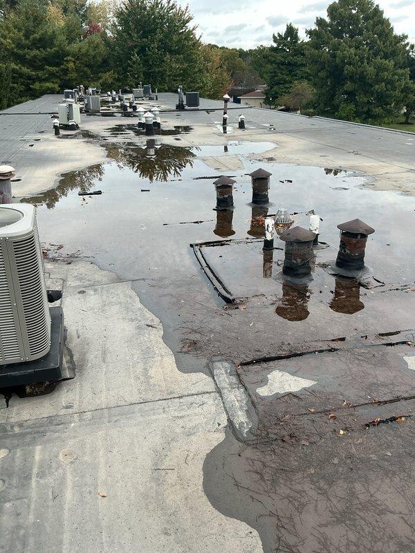 Responded to no cooling complaint with water leaking through ceiling from recently installed Lennox rooftop unit. Upon inspection, found extensive standing water pooling on flat commercial roof surface due to inadequate drainage, with debris accumulation around multiple roof penetrations and HVAC equipment. Documented significant roofing membrane deterioration, compromised drainage system, and water intrusion points near unit installation. Identified warranty-covered equipment as potential source of condensate leak contributing to ceiling water damage. Photographed roof conditions, standing water patterns, unit installation, refrigerant line connections showing weathering, and drainage deficiencies for warranty claim documentation and recommended immediate roof drainage remediation to prevent further water intrusion and equipment damage.