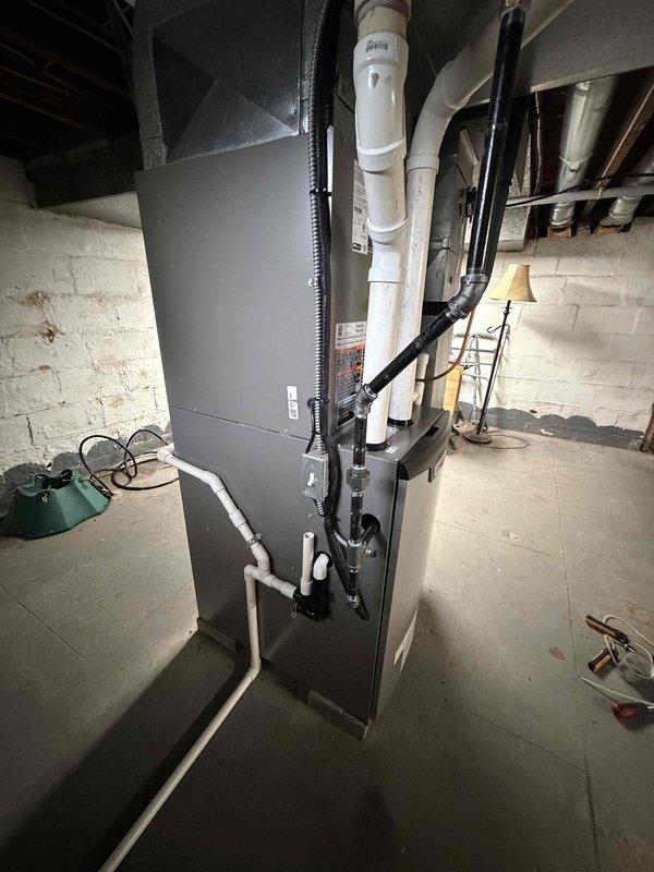 # HVAC Install - Complete System

Completed installation of a 90% efficiency furnace and air conditioning system at residential property. Installed new dark gray air handler unit in basement utility room with proper vertical positioning and clearances. Ran white PVC condensate drain lines and installed black electrical conduit to unit per code requirements. Connected unit to existing ductwork system in basement mechanical room.

Exterior work included placement of beige/tan air conditioning condenser unit on ground pad adjacent to building. Mounted gray electrical disconnect box on exterior wall with proper wiring connections. Ran copper refrigerant lines from condenser to indoor air handler, completing refrigerant circuit between components. System tested and confirmed operational with proper airflow and temperature differential across both heating and cooling modes.