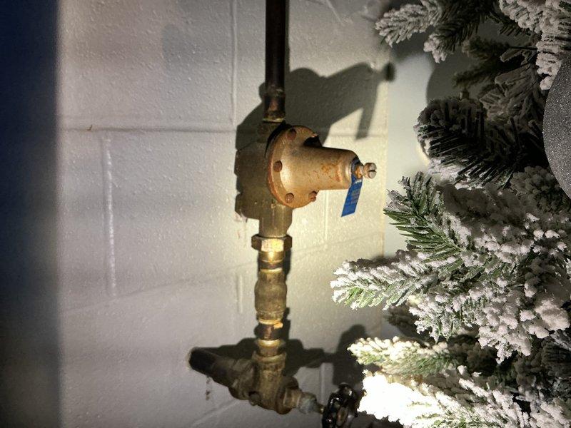 Responded to service call for water heater leaking approximately half cup of water daily. Upon inspection, identified leak originating from pressure relief valve assembly. Photographed existing plumbing configuration showing copper supply lines, brass fittings, and T&P relief valve with discharge tube. Placed collection bucket beneath leak point to contain water discharge. Documented condition of water heater connections, shutoff valves, and surrounding plumbing infrastructure for repair assessment and customer records.