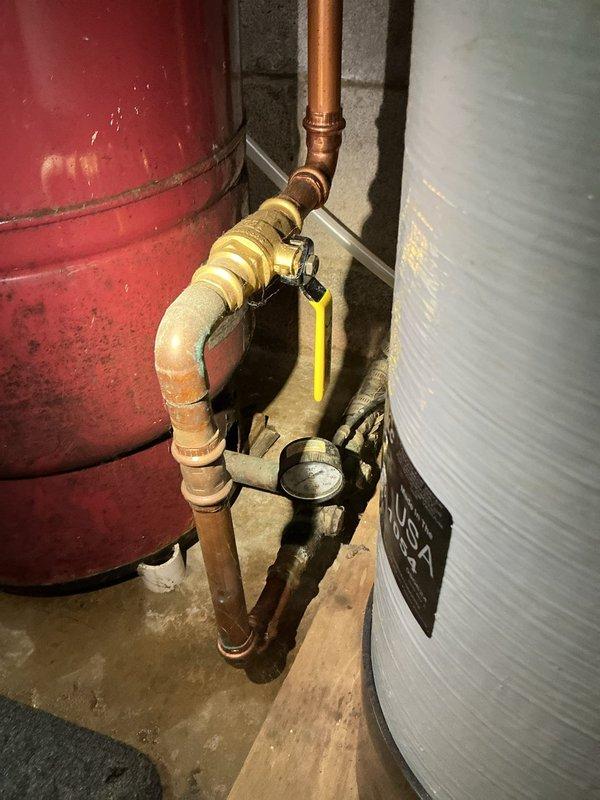 Responded to emergency water leak in basement originating from failed pressure tank near water softener system. Upon arrival, confirmed homeowner had shut off well pump breaker to stop active high-pressure spray, leaving property without running water. Performed diagnostic inspection and identified compromised pressure tank requiring replacement. Documented existing plumbing configuration including copper supply lines, ball valve assembly, and connections to water heater system. Assessed installation requirements and confirmed proper replacement supplies needed for pressure tank swap-out to restore water service before guests' arrival.