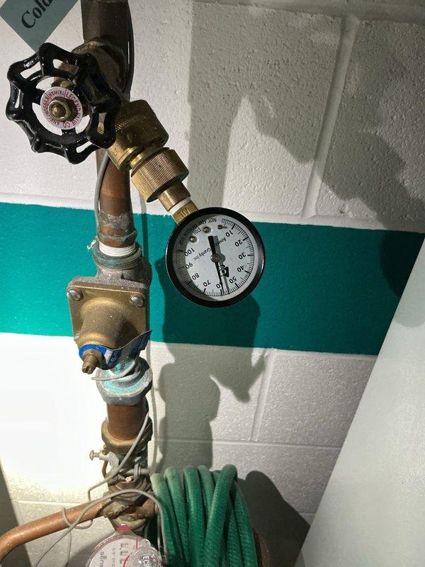 Responded to customer complaint of rattling and banging noises occurring intermittently during washing machine fill cycles and occasionally when shower is running. Upon arrival, inspected main water supply plumbing system and identified water hammer condition caused by inadequate air cushioning in the supply lines. Examined vertical copper pipe assembly including main shutoff valve, pressure regulator, and associated brass fittings for proper operation and secure mounting. Verified pressure gauge readings were within normal parameters and confirmed all compression fittings and connections were tight with no visible leaks. Assessed condition of existing plumbing infrastructure, noting aged copper piping with minor surface oxidation but structurally sound. Documented installation with photographs showing complete plumbing assembly, pressure regulation equipment, and valve configuration for service records.