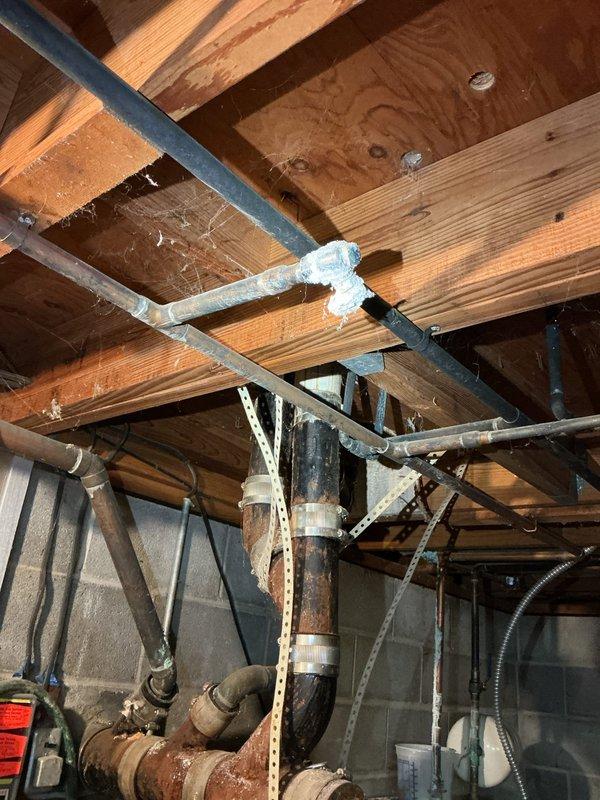 Responded to service call for leaking pipes in utility area. Upon inspection, identified deteriorated horizontal PVC pipe with visible staining and corrosion on metal fittings. Assessed vertical plumbing assembly and overhead pipe runs in basement area, noting aged infrastructure with rust accumulation on support column and compromised insulation wrapping on sections of piping. Documented conditions of all affected plumbing components and provided recommendations for necessary repairs to address active leaks and prevent future failures in the aging system.