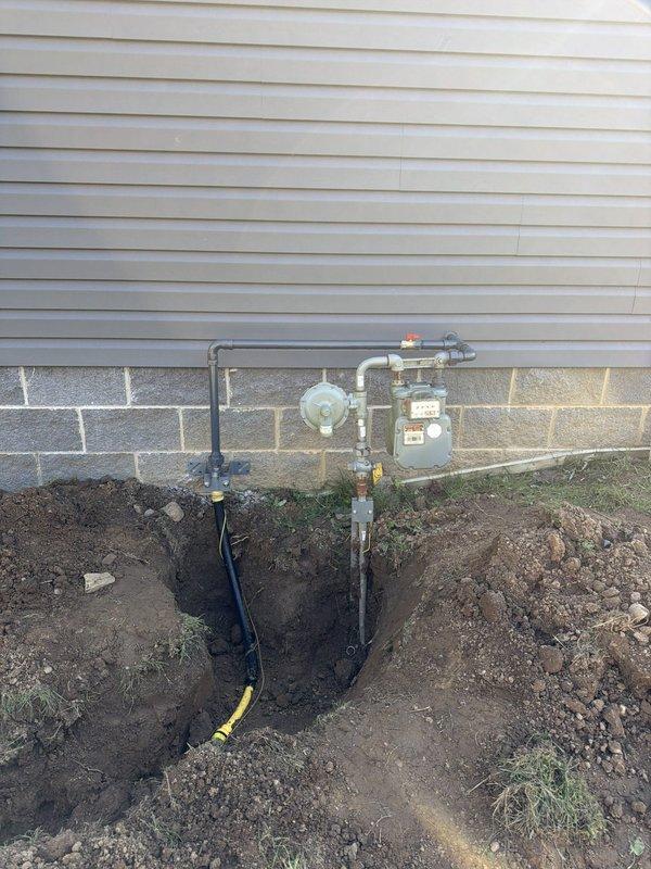 Installed dual gas line system from existing meter to backyard patio area for future gas fireplace and outdoor kitchen. Mounted wall bracket on left side of gas meter, tapped into existing 1-inch line with tee fitting and new shut-off valve. Ran underground gas lines to two separate locations in backyard, installing underground tee to split service. Installed 3-inch PVC sleeves at both riser locations for protection. Reduced each line to 1/2-inch pipe at termination points and installed gas shut-off valves with plugs. Contractor provided trench excavation to minimum 18-inch depth and backfill services.