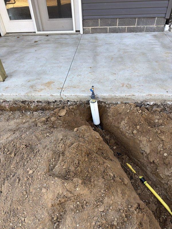 Installed dual gas line system from existing meter to backyard patio area for future gas fireplace and outdoor kitchen. Mounted wall bracket on left side of gas meter, tapped into existing 1-inch line with tee fitting and new shut-off valve. Ran underground gas lines to two separate locations in backyard, installing underground tee to split service. Installed 3-inch PVC sleeves at both riser locations for protection. Reduced each line to 1/2-inch pipe at termination points and installed gas shut-off valves with plugs. Contractor provided trench excavation to minimum 18-inch depth and backfill services.