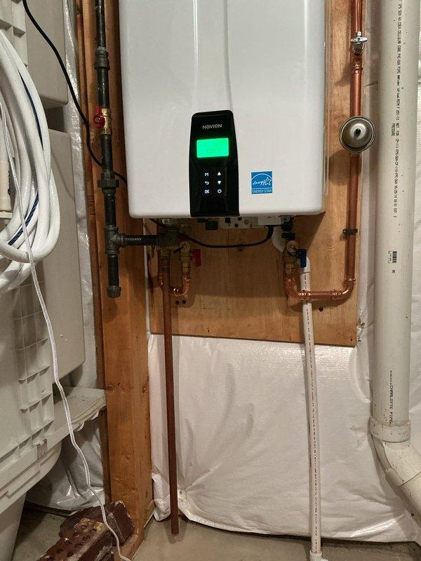 Removed existing tank-style water heater and installed new Navien NPE240A2 tankless water heater, wall-mounted in previous tank location. Rerouted water supply and gas lines to accommodate wall-mounted configuration with new copper piping and necessary valves and fittings. Installed condensate drain line routing to existing floor drain, ran new exhaust vent line exiting southwest side of home, and repurposed existing power vent exhaust penetration for fresh air intake line. Mounted unit on backing board between wall studs with proper clearances, completed all electrical connections, pressure tested system, and verified proper operation of unit with digital display functioning correctly.