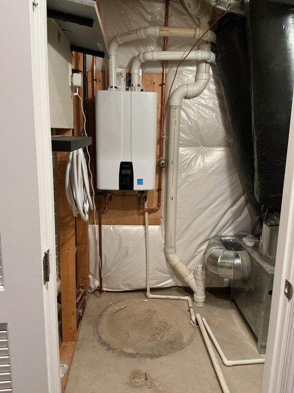 Removed existing tank-style water heater and installed new Navien NPE240A2 tankless water heater, wall-mounted in previous tank location. Rerouted water supply and gas lines to accommodate wall-mounted configuration with new copper piping and necessary valves and fittings. Installed condensate drain line routing to existing floor drain, ran new exhaust vent line exiting southwest side of home, and repurposed existing power vent exhaust penetration for fresh air intake line. Mounted unit on backing board between wall studs with proper clearances, completed all electrical connections, pressure tested system, and verified proper operation of unit with digital display functioning correctly.