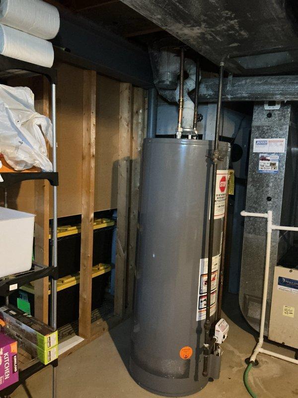 Responded to service call for natural gas water heater that was disconnected due to roofing work in progress. Upon arrival, assessed water heater location in basement mechanical room and evaluated existing venting configuration. Determined that venting system requires rerouting through attic space to accommodate roofing modifications and establish proper termination point at new location. Documented current equipment setup and storage area conditions with photographs showing water heater positioned between wall framing and HVAC unit, with copper supply lines connected at top. Provided customer with assessment and recommendations for venting reinstallation once roofing work is completed.