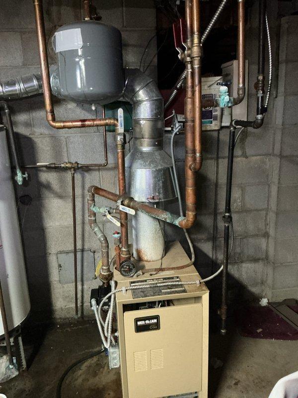 Responded to service call for leaking expansion tank on Weil-McLain CGA-5 hot water boiler installed in 2018. Upon arrival, found Amtrol EX-30 expansion tank with visible penetration in tank surface that had been temporarily patched with tape. Tank was actively leaking and required replacement to prevent system damage and maintain proper pressure regulation. Removed failed expansion tank and installed new Amtrol EX-30 expansion tank with proper pre-charge pressure of 12 PSI. Connected new tank to existing copper piping system, verified all connections for leaks, and confirmed boiler operation. System tested and confirmed functioning properly with no leaks detected.