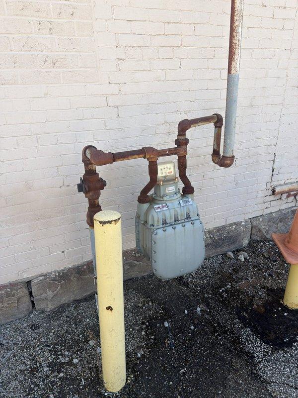 Performed site assessment and provided estimate for installation of natural gas line to power standby generator. Evaluated existing gas meter location and determined optimal routing path from meter assembly to proposed generator placement area. Documented current gas infrastructure including aged copper piping with visible corrosion and patina, existing meter connections, and protective bollards. Assessed wall penetration requirements through white brick exterior and measured distances for material calculations. Generator unit to be supplied by property owner. Provided comprehensive estimate covering gas line installation, required fittings, pressure testing, and connection specifications per local code requirements.