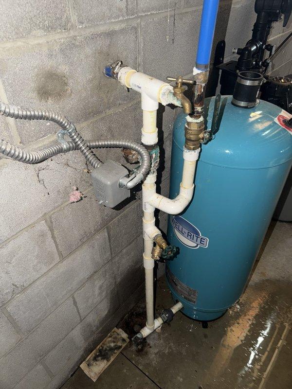 Responded to service call for reported water leak near water treatment equipment. Upon inspection, determined that the water softener and pressure tank system were not the source of the leak. Located actual leak source in ceiling above the water softener, where plumbing connections showed signs of water discharge. Documented conditions with photographs showing standing water on basement floor around equipment and identified overhead piping with PEX and PVC connections requiring attention. Customer unable to access basement for personal inspection due to mobility constraints.