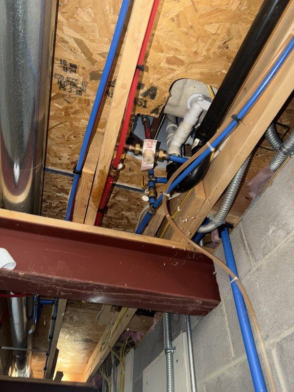 Responded to service call for reported water leak near water treatment equipment. Upon inspection, determined that the water softener and pressure tank system were not the source of the leak. Located actual leak source in ceiling above the water softener, where plumbing connections showed signs of water discharge. Documented conditions with photographs showing standing water on basement floor around equipment and identified overhead piping with PEX and PVC connections requiring attention. Customer unable to access basement for personal inspection due to mobility constraints.