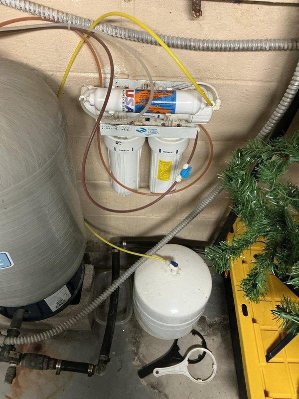 Responded to service call for reverse osmosis system with reduced storage capacity in 11-year-old residential installation. Performed comprehensive inspection of RO system components including pre-filters, membrane housing, storage tank, and pressure settings. Evaluated system performance and identified aging storage tank with diminished capacity as primary issue. Documented existing filtration setup with two-stage pre-filtration and horizontal membrane cartridge configuration. Assessed overall system condition, noting regular filter maintenance history with replacements every six months. Photographed installation for reference including storage tank, filter housings, tubing connections, and mounting configuration in basement utility area. Provided recommendations to customer regarding repair versus replacement options based on system age and component condition.