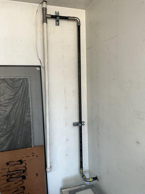 Responded to failed inspection requiring code compliance corrections for gas line installation. Installed proper metal mounting straps and brackets to secure black gas piping running vertically along interior wall, ensuring adequate support per local code requirements. Added necessary clamp-style brackets at appropriate intervals to eliminate unsupported spans. Gas line routing includes vertical run with 90-degree bend transitioning to horizontal connection at utility box. All mounting hardware properly fastened to wall structure to prevent pipe movement and maintain system integrity.