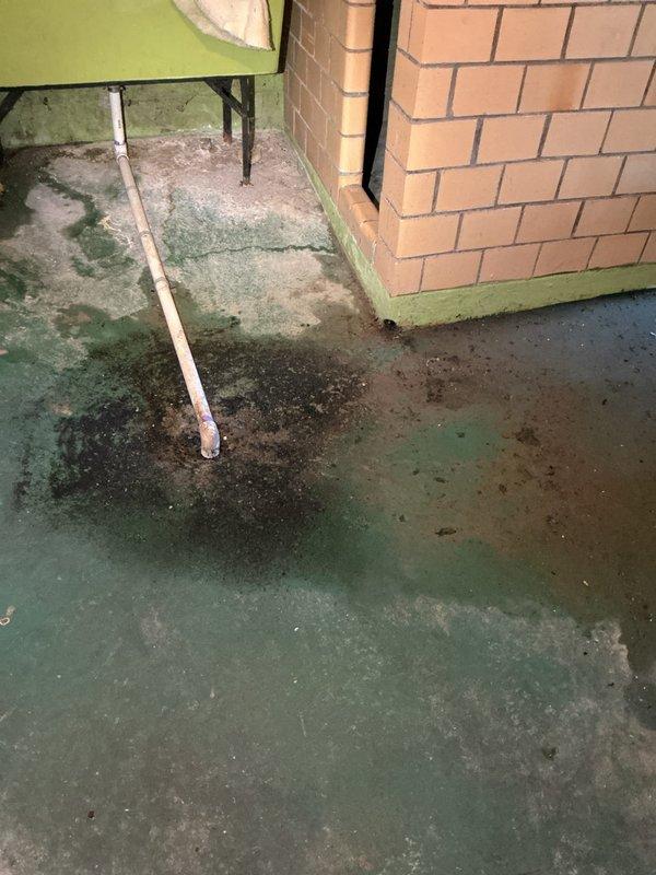 Responded to a report of water backing up from the basement floor drain with standing water around the drain, and performed a diagnostic inspection of the floor drain and connected drain piping. Findings showed heavy staining and moisture at the drain area, along with a severely corroded drain fitting and rusted pipe rim with mineral deposits and debris buildup, indicating a deteriorated drain connection and restricted flow. Documented conditions with photos and recommended further drain clearing and repair or replacement of the corroded components.