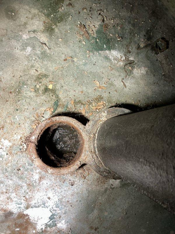 Responded to a report of water backing up from the basement floor drain with standing water around the drain, and performed a diagnostic inspection of the floor drain and connected drain piping. Findings showed heavy staining and moisture at the drain area, along with a severely corroded drain fitting and rusted pipe rim with mineral deposits and debris buildup, indicating a deteriorated drain connection and restricted flow. Documented conditions with photos and recommended further drain clearing and repair or replacement of the corroded components.