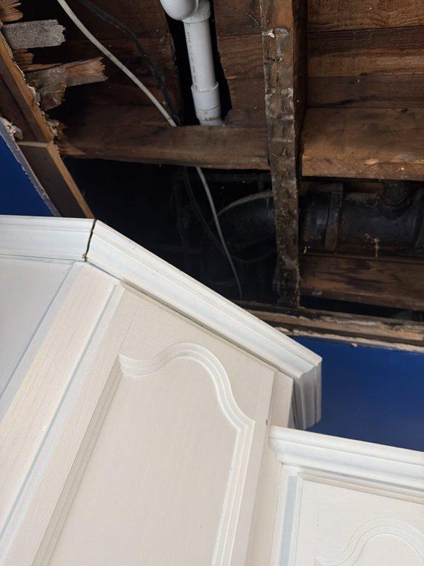 Inspected the open kitchen ceiling cavity to trace an intermittent leak and found moisture-stained framing around the cast iron drain assembly beneath the upstairs toilet, including the banded coupling and elbow transitions to the PVC drain line. Repaired the leaking connections at the toilet drain pipe and verified the bathtub drain repair, restoring a watertight drain system. Documented the exposed plumbing and water-damaged joists for follow-up ceiling restoration.