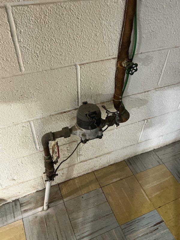 Performed an on-site assessment of the tanked water heater replacement, inspecting the water supply piping, shutoff valves, and surrounding utility connections. Noted corroded copper and steel supply piping with heavy oxidation, a gate valve and ball valve on the supply line, and staining on the subfloor framing above the valve assembly, which may indicate prior moisture exposure. Documented existing conditions with photos and prepared the replacement scope, including the water meter assembly, supply lines, and electrical connections near the unit.