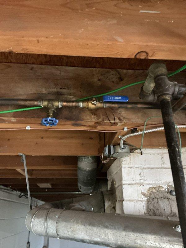 Performed an on-site assessment of the tanked water heater replacement, inspecting the water supply piping, shutoff valves, and surrounding utility connections. Noted corroded copper and steel supply piping with heavy oxidation, a gate valve and ball valve on the supply line, and staining on the subfloor framing above the valve assembly, which may indicate prior moisture exposure. Documented existing conditions with photos and prepared the replacement scope, including the water meter assembly, supply lines, and electrical connections near the unit.