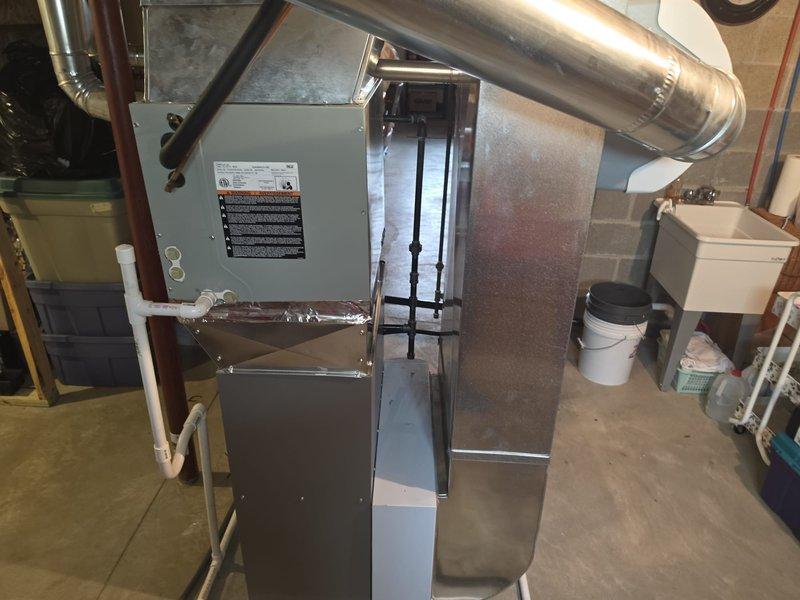 Installed a new Lennox upright gas furnace in the basement mechanical area, connecting it to the existing galvanized supply plenum and ductwork with a new sheet metal transition. Completed the black iron gas piping with unions, routed the PVC condensate drain, and connected the flue vent with foil-taped joints and electrical wiring, leaving the system ready for operation.