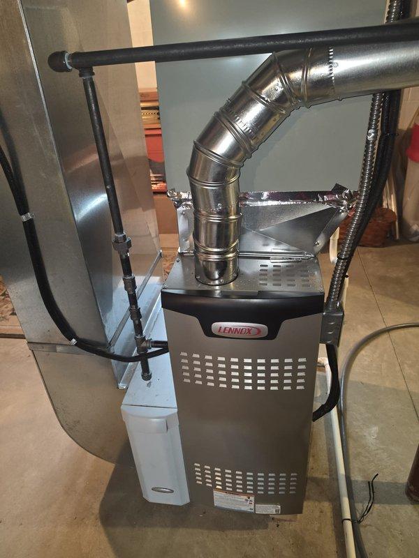 Installed a new Lennox upright gas furnace in the basement mechanical area, connecting it to the existing galvanized supply plenum and ductwork with a new sheet metal transition. Completed the black iron gas piping with unions, routed the PVC condensate drain, and connected the flue vent with foil-taped joints and electrical wiring, leaving the system ready for operation.