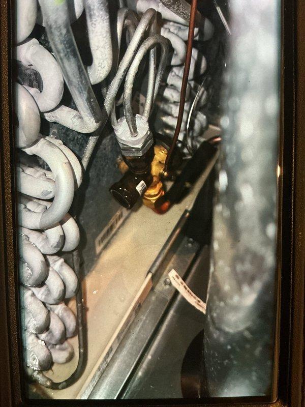Performed seasonal heating maintenance on a 2-year-old furnace system, including inspection of the furnace and associated air handler components. Observed heavy frost and ice accumulation on the evaporator coil and expansion valve area, indicating a possible airflow restriction or refrigerant charge issue, and verified the condensate drain pan, PVC drain line, and refrigerant line insulation connections were intact with no visible rust or leaks. Recommend further diagnostics of the evaporator coil icing condition to determine root cause and prevent recurrence.