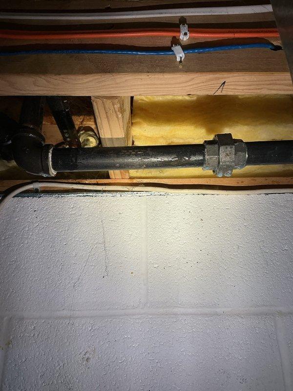 Performed leak detection on the interior gas piping using bubble solution and located an active leak at a threaded coupling on the black iron gas line in the basement joist cavity, with surface corrosion and pitting noted on the adjacent pipe. The affected section was identified for repair, and the remaining accessible gas piping, including the elbow and union fittings, was inspected for additional leaks.