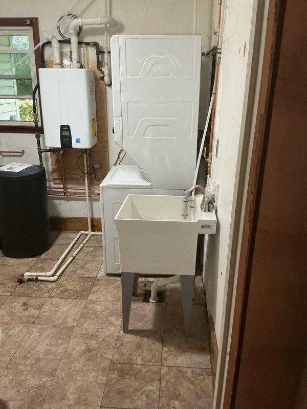 Installed a Navien NPE-240A2 condensing tankless water heater with the Nav/Rin kit, including new venting, water supply, and condensate drain piping. Installed a sanitizer water softener with brine tank and tubing, and set up a freestanding utility sink with faucet, drain connection, and laundry hookups for the washer.