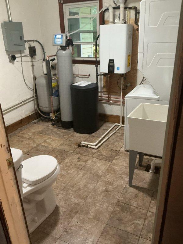 Installed a Navien NPE-240A2 condensing tankless water heater with the Nav/Rin kit, including new venting, water supply, and condensate drain piping. Installed a sanitizer water softener with brine tank and tubing, and set up a freestanding utility sink with faucet, drain connection, and laundry hookups for the washer.