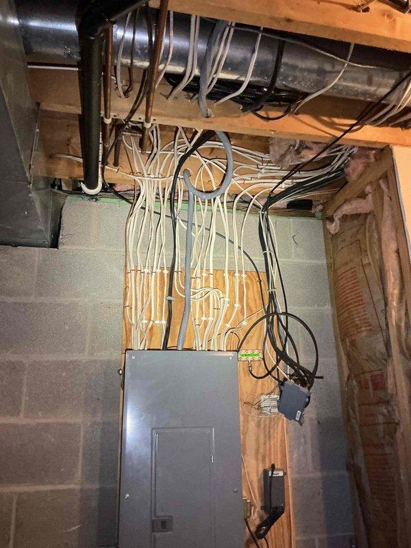 Performed an on-site evaluation for a new home generator installation, with no existing generator or related equipment present. Inspected the main electrical panel and surrounding service area in the unfinished basement, noting dense low-voltage and branch cabling routed through the ceiling joists and along the plywood panel backing, along with nearby ductwork, piping, and exposed wall cavity insulation that will need to be considered for conduit routing and transfer switch placement. Documented existing conditions with photos to support estimate preparation.