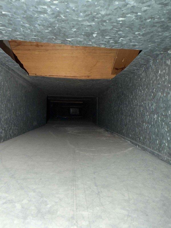 Performed duct cleaning on the galvanized sheet metal supply trunk, removing accumulated dust, debris, and reddish-brown residue from the duct floor and seams. Inspected the interior and documented a section of broken wood paneling at the duct ceiling opening, recommending repair or replacement to restore system integrity and airflow.
