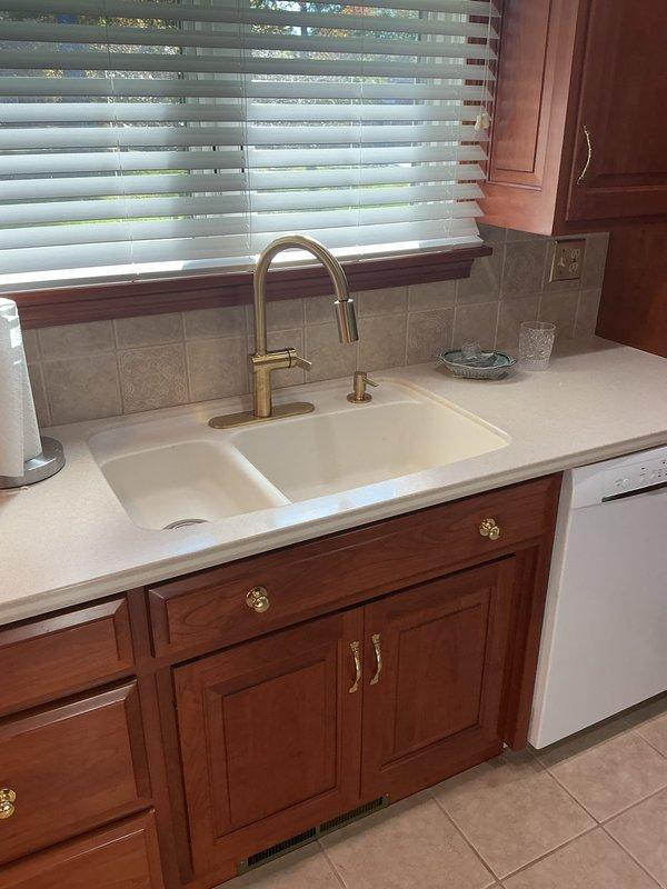 Removed the existing kitchen faucet and installed a new brushed gold pull-down gooseneck faucet at the double-basin sink, then replaced both bathroom vanity faucets with new lever-handle units. Reconnected all supply lines, tested each fixture for proper operation and leaks, and left the work areas clean with all fixtures functioning correctly.