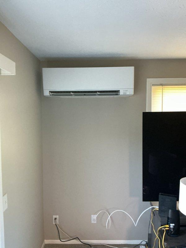 Installed a single-zone ductless mini-split system, mounting the outdoor condenser on a level timber platform at grade and the wall-mounted indoor air handler high on the interior wall. The line set was run through the exterior wall in conduit with insulated refrigerant lines and power/communication cable, and the equipment was left in clean, undamaged condition with no visible frost, rust, or defects.