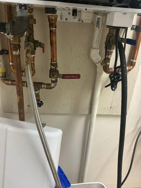 Performed a descale flush of the tankless water heater by isolating the unit at the service valves and circulating descaling solution through the heat exchanger to remove mineral buildup, then flushed the system with clean water and restored normal operation. Removed the saddle valve feeding the humidifier, which had not been addressed during the original installation, and capped the connection to eliminate a potential leak point. Noted corrosion and rust staining on the braided flex connector and brass fittings, which should be monitored for future replacement.