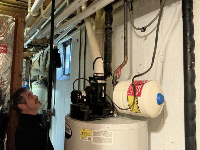 Performed an on-site estimate for replacing the existing power-vent tank-style water heater with a tankless unit, and evaluated relocating a furnace to the garage. Inspected the existing Smith water heater, PVC exhaust venting, expansion tank, copper supply piping with isolation valve, condensate/drain routing, and electrical connections, and found no visible leaks, rust, or damage. Documented the mechanical room layout with photos to determine gas, venting, and water line requirements for the tankless installation.