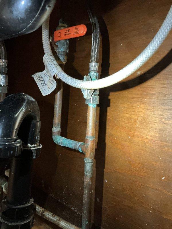 Responded to a callback for leaking and dripping at a recently installed utility sink and two faucets. Inspected the under-sink supply and drain assemblies and found heavy verdigris corrosion and mineral buildup at the soldered copper joints, angle stop valve, and base flange, along with slip-joint connections on the P-trap and flexible supply lines as potential leak points. Documented all findings with photos.