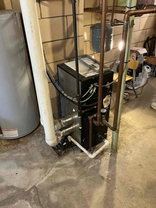 Performed an on-site evaluation of the existing boiler installation in the basement mechanical area to prepare a replacement estimate. Inspected the boiler and surrounding components, including the expansion tank, circulator, copper and black iron supply piping, PVC condensate drain and trap, and exhaust venting, and documented the system with photos. Noted staining and dampness on the concrete floor near the base of the PVC drain, which should be checked for condensate or leak issues during the replacement scope.
