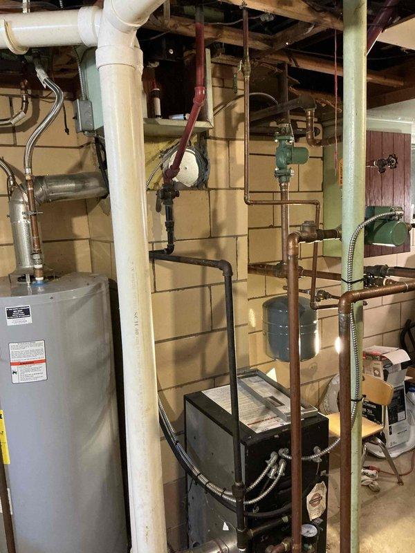 Performed an on-site evaluation of the existing boiler installation in the basement mechanical area to prepare a replacement estimate. Inspected the boiler and surrounding components, including the expansion tank, circulator, copper and black iron supply piping, PVC condensate drain and trap, and exhaust venting, and documented the system with photos. Noted staining and dampness on the concrete floor near the base of the PVC drain, which should be checked for condensate or leak issues during the replacement scope.