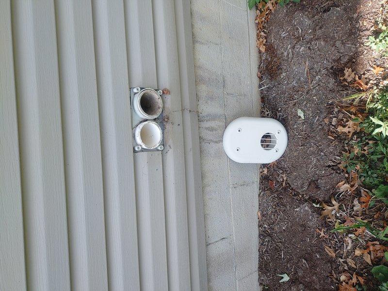 Located the detached louvered exterior vent cover from the recently installed furnace and reinstalled it on the exterior wall at the combustion air/vent termination, securing it with screws. Verified the PVC intake and exhaust terminations were properly seated in the mounting plate and free of obstruction.
