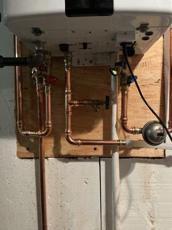 Installed a Navien tankless water heater on a plywood backer board mounted to the masonry wall, with new press-fit copper supply and return piping, isolation valves for service flushing, and an expansion tank. Terminated the PVC venting and condensate/combustion piping through the exterior brick wall, then verified that all connections were secure and leak-free.