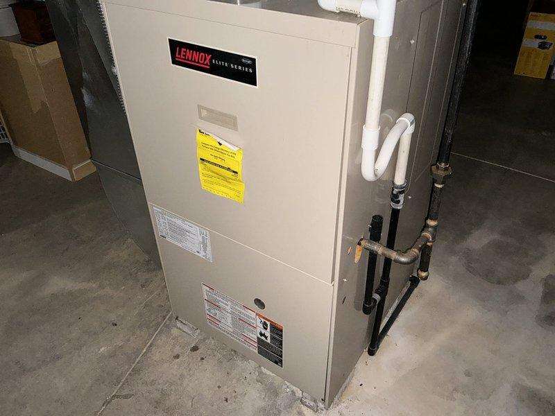 Performed an on-site estimate for replacement of an existing Lennox Elite Series upright gas furnace, documenting the unit's data plate, gas piping, PVC condensate/venting, and surrounding ductwork configuration. Assessed the unfinished basement installation, noting adequate clearances, exposed overhead duct and piping runs, and signs of moisture on the adjacent block wall, and photographed all conditions to support equipment sizing and replacement scope.
