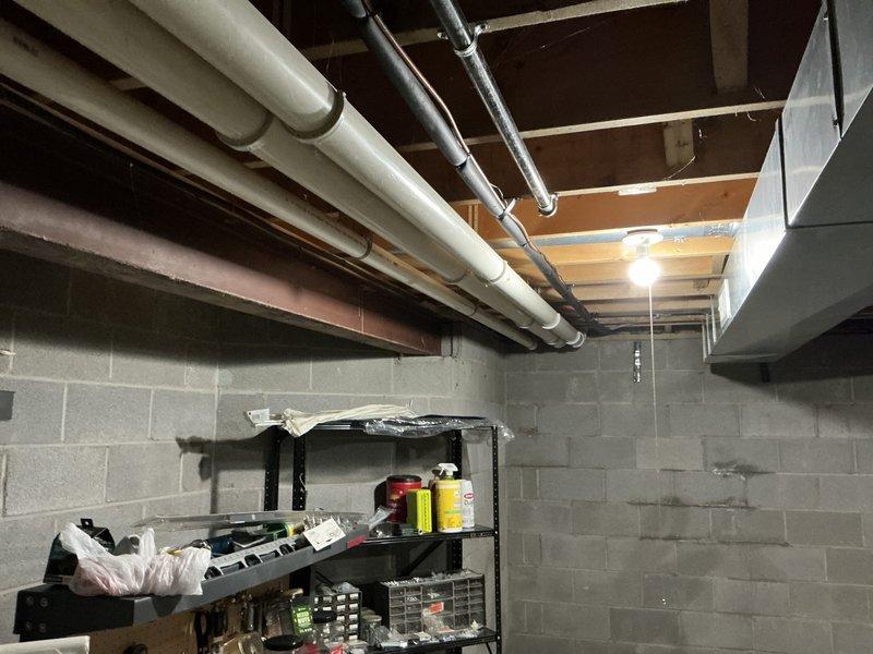 Performed an on-site estimate for replacement of an existing Lennox Elite Series upright gas furnace, documenting the unit's data plate, gas piping, PVC condensate/venting, and surrounding ductwork configuration. Assessed the unfinished basement installation, noting adequate clearances, exposed overhead duct and piping runs, and signs of moisture on the adjacent block wall, and photographed all conditions to support equipment sizing and replacement scope.