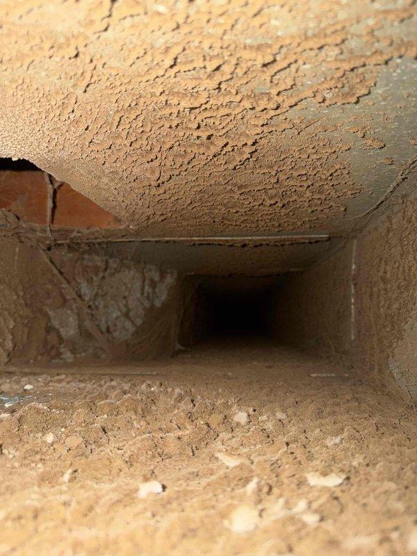 Performed a complete duct cleaning on a ranch-style home's supply and return system (under 14 vents), removing heavy accumulations of dust, debris, and cobwebs from the trunk lines and branch runs. Documented severely deteriorated duct lining and a breach in the duct wall exposing the masonry beneath, and recommended repair or replacement of the damaged sections to prevent further debris intrusion and air leakage.