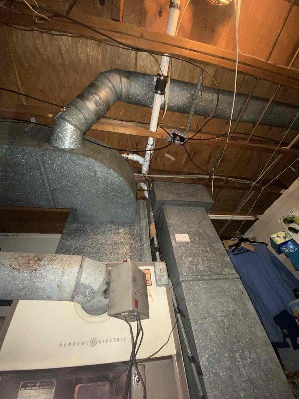 Conducted assessment of obsolete oil furnace system (approximately 60 years old) in confined utility space. General Electric air handler unit observed with extensive metal ductwork covered in gray insulation. System has not received maintenance for approximately 2 years. Recommended full replacement due to equipment age and inefficiency.