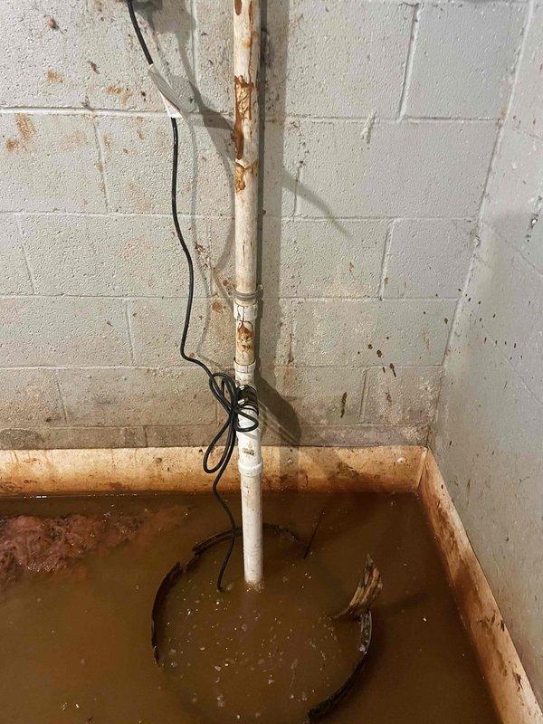 Responded to service call for a non-functioning sump pump causing water accumulation in the basement. Inspection revealed significant rust deterioration on the vertical PVC discharge pipe with visible water staining on surrounding concrete blocks. Replaced failed sump pump unit and checked system functionality to ensure proper water evacuation from the pit.