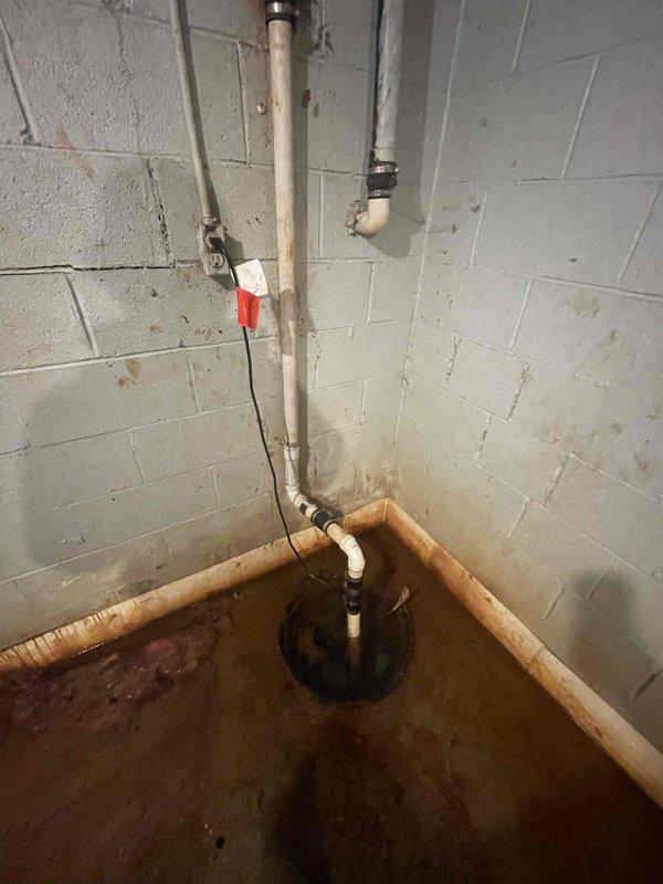 Responded to service call for a non-functioning sump pump causing water accumulation in the basement. Inspection revealed significant rust deterioration on the vertical PVC discharge pipe with visible water staining on surrounding concrete blocks. Replaced failed sump pump unit and checked system functionality to ensure proper water evacuation from the pit.