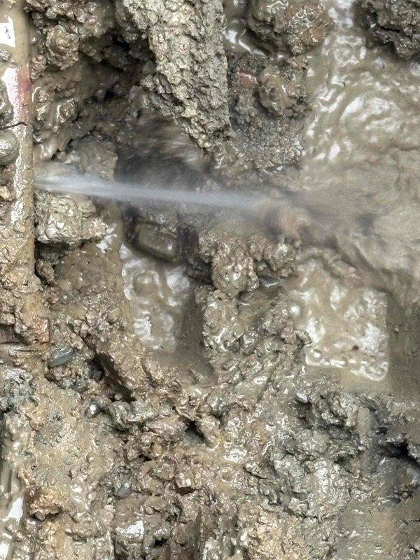 Excavated exterior area to access leaking water line. Located and repaired damaged section of pipe causing visible water spray from ground. Installed new copper piping with brass shutoff valve and connected to existing water filtration system mounted on concrete block wall.
