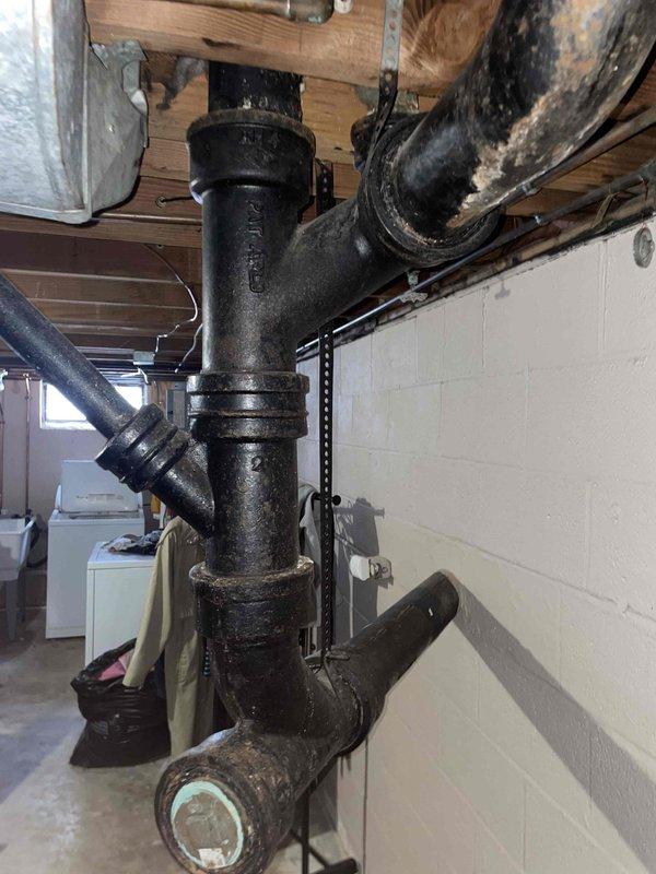 Responded to recurring toilet leak issue affecting basement area. Diagnosed clog in main cleanout of cast iron drain pipe system. Cleared obstruction and inspected T-junction connections for proper function. Noted water damage on basement wall requiring monitoring for potential mold development.